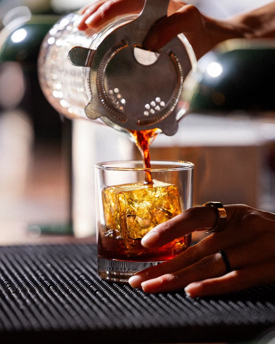 A cocktail being poured over a single large ice cube.