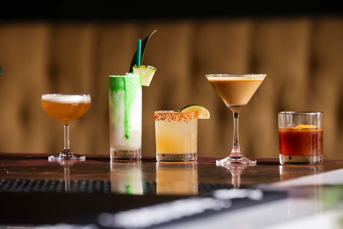 Five cocktails lined up across the bar top.