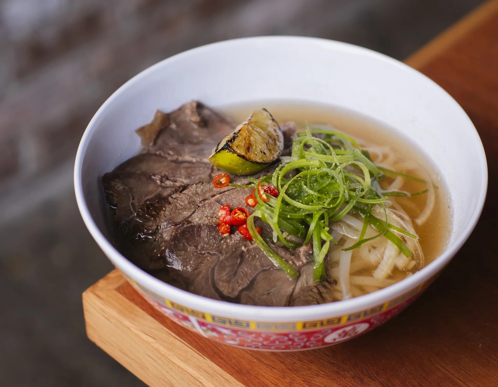 A bowl of rare-beef pho on a printed placemat.